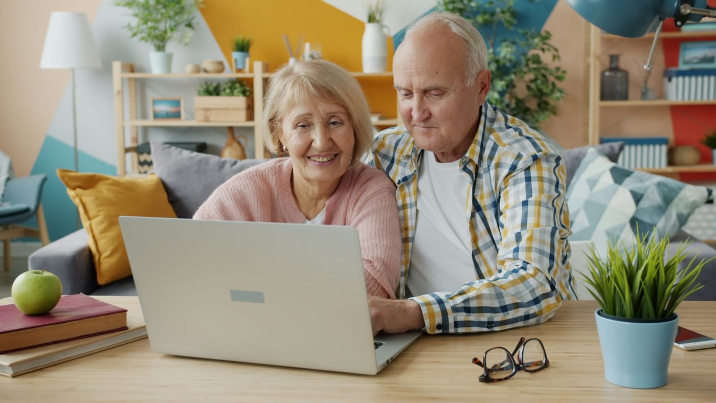 An older couple smile together as they look at a laptop.